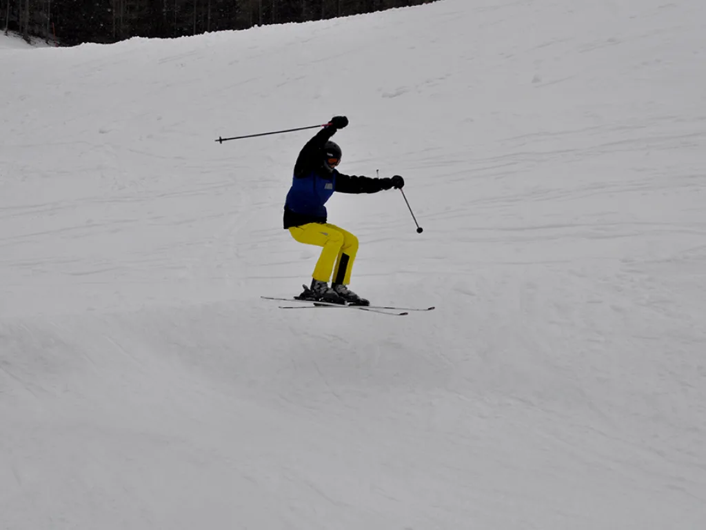 Skifahrer in gelber Hose zieht einen Schwung.